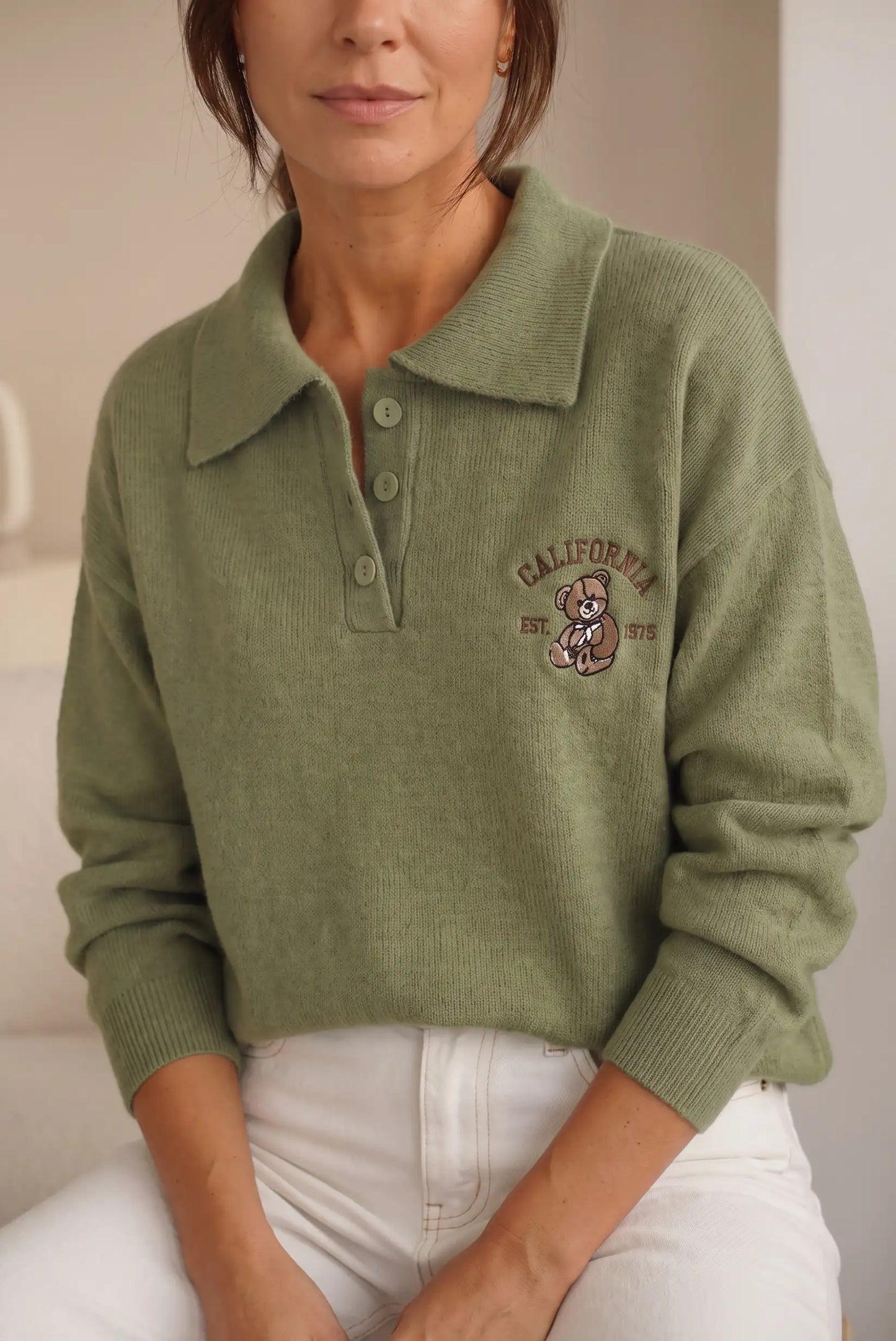 Mujer vistiendo jersey de punto verde oliva con cuello polo y bordado de oso.