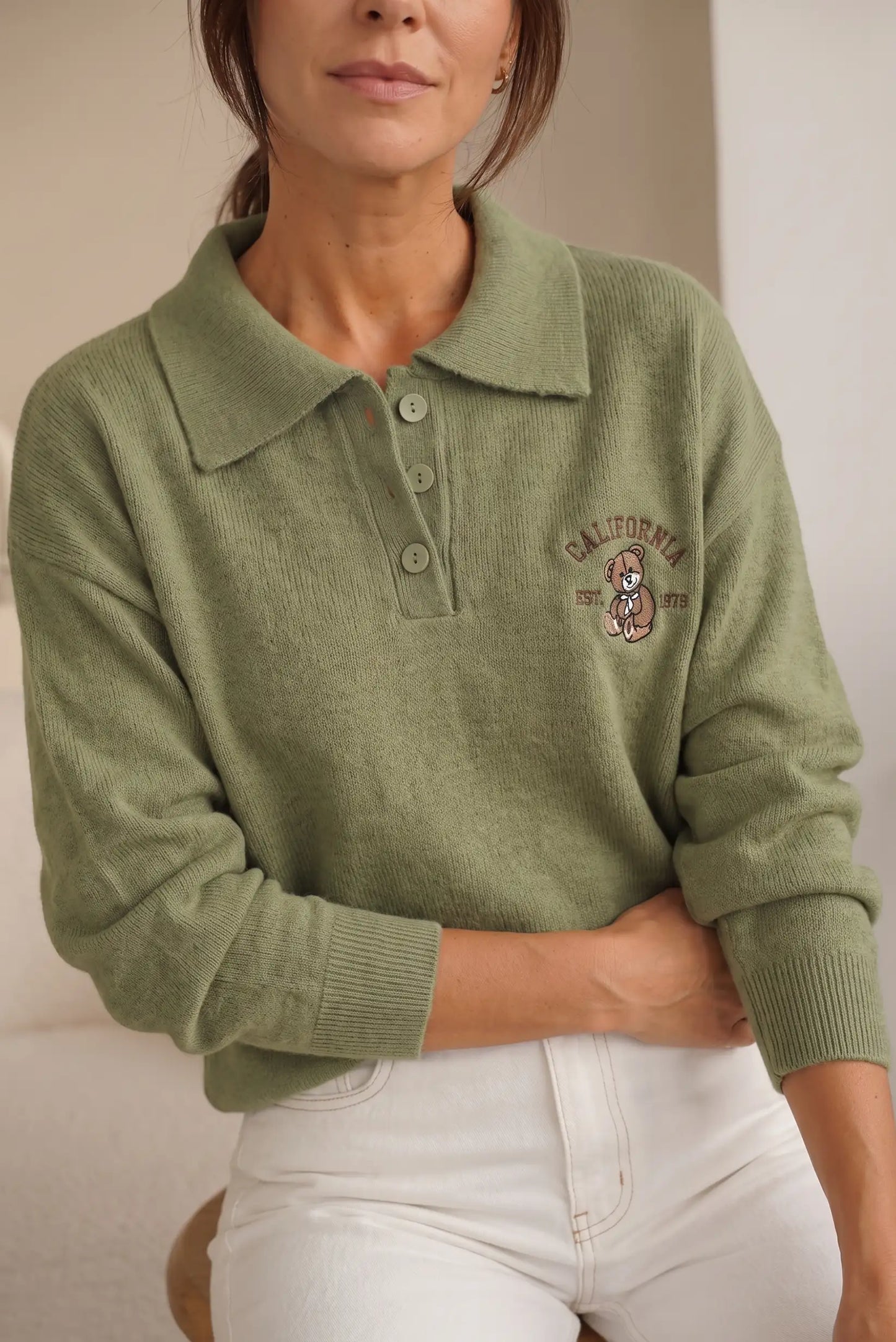 Mujer vistiendo un jersey de punto color verde oliva con cuello polo y bordado de California.