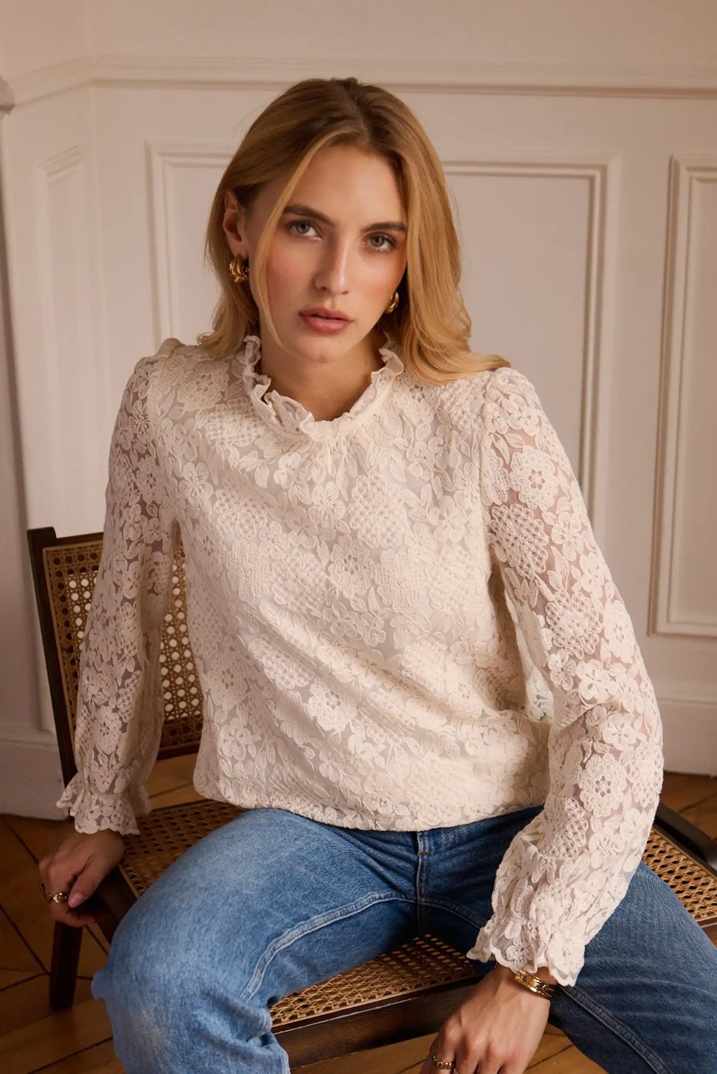 Blusa de encaje blanco con mangas largas y cuello fruncido, combinada con jeans azules, ideal para looks femeninos y elegantes.