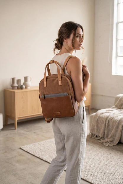 Mujer de perfil con mochila de cuero marrón y pantalones blancos en interior luminoso.