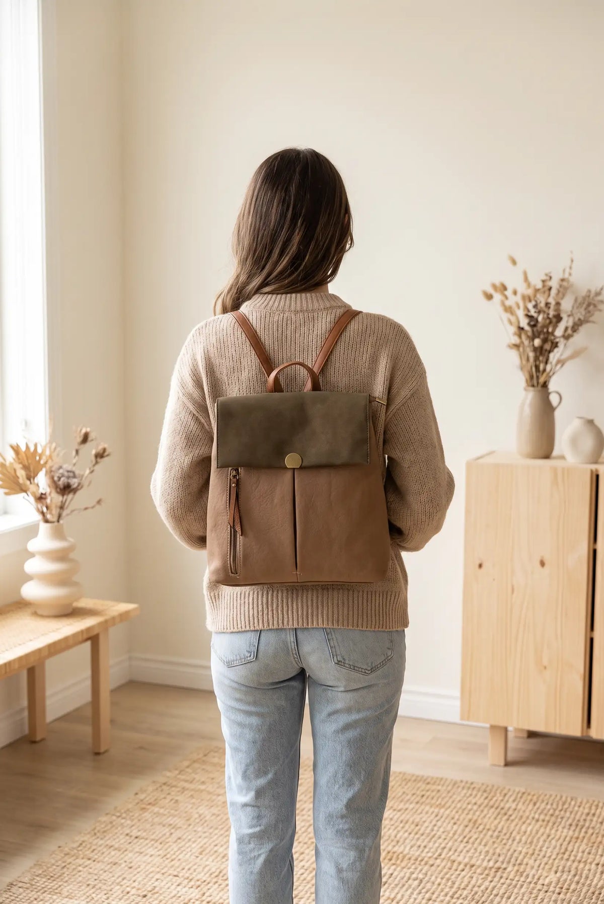 Mujer de espaldas con jersey beige y mochila de cuero marrón y verde oliva