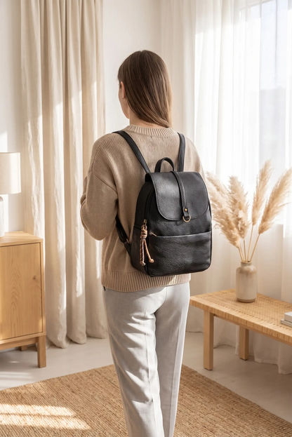 Mujer de espaldas con mochila de cuero negro, jersey beige y pantalones blancos.