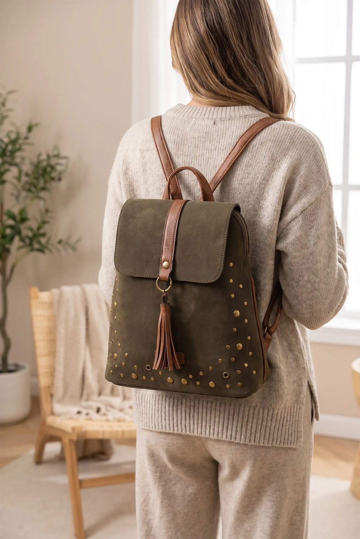Mujer de espaldas con jersey beige y mochila de gamuza verde oliva con detalles dorados