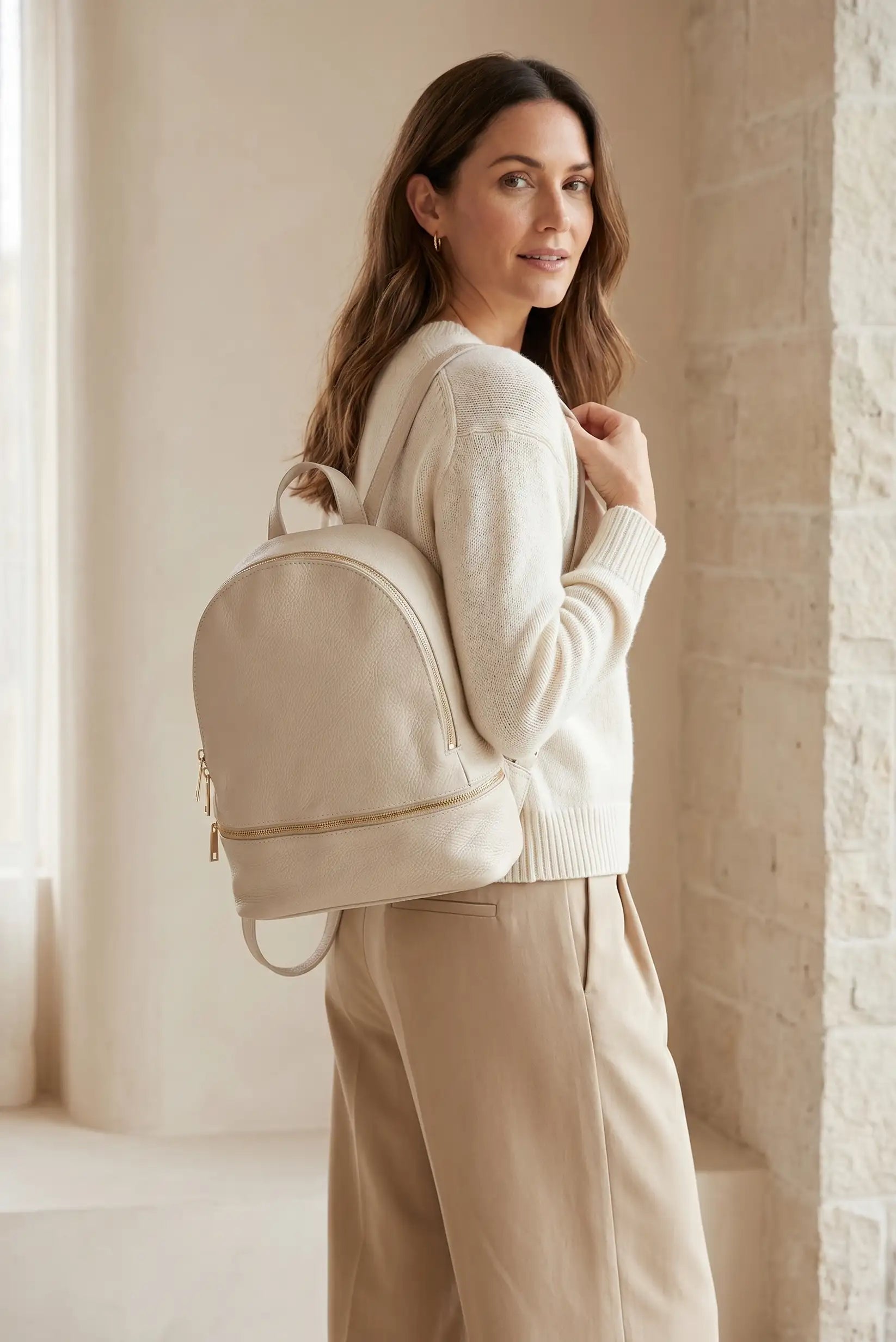 Mujer con mochila urbana de cuero beige, look casual y elegante, fondo interior luminoso.