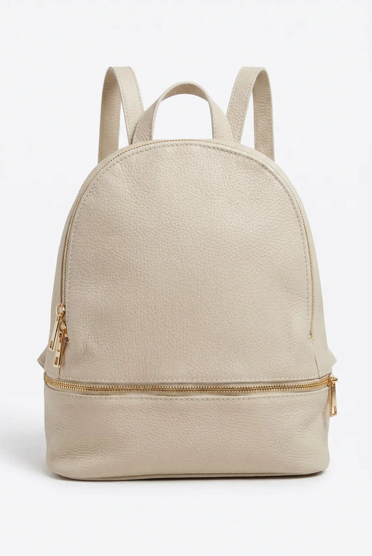 Mochila urbana de mujer en cuero beige con cremalleras doradas, estilo casual moderno.