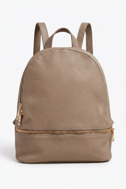 Mochila urbana de mujer color taupe de cuero con cremalleras doradas, fondo blanco.