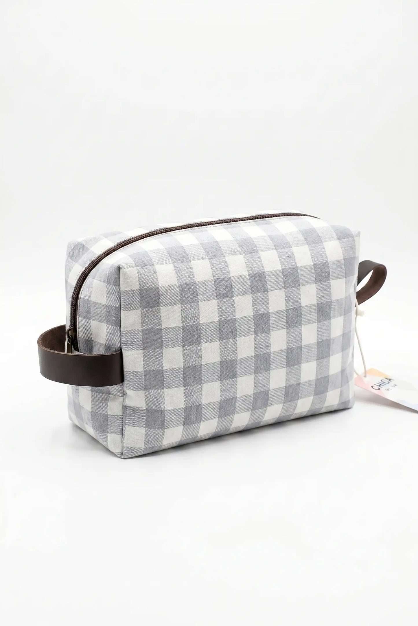 Neceser de tela con estampado de cuadros vichy gris y blanco, detalles en cuero marrón.