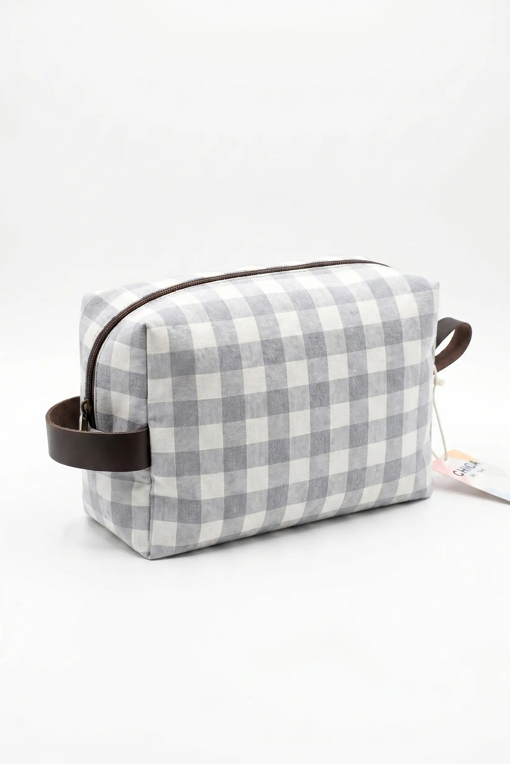 Neceser de tela con estampado de cuadros vichy gris y blanco, detalles en cuero marrón.