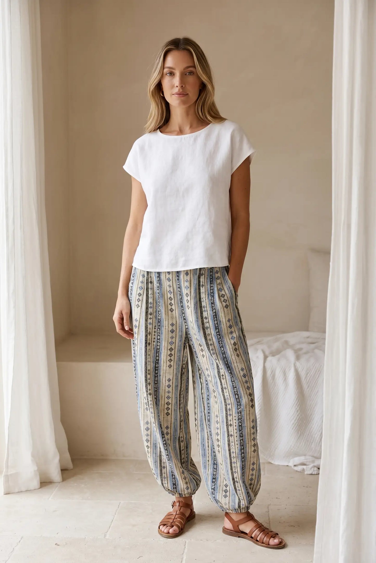 Mujer con pantalón bombacho largo azul étnico y blusa blanca casual en ambiente minimalista