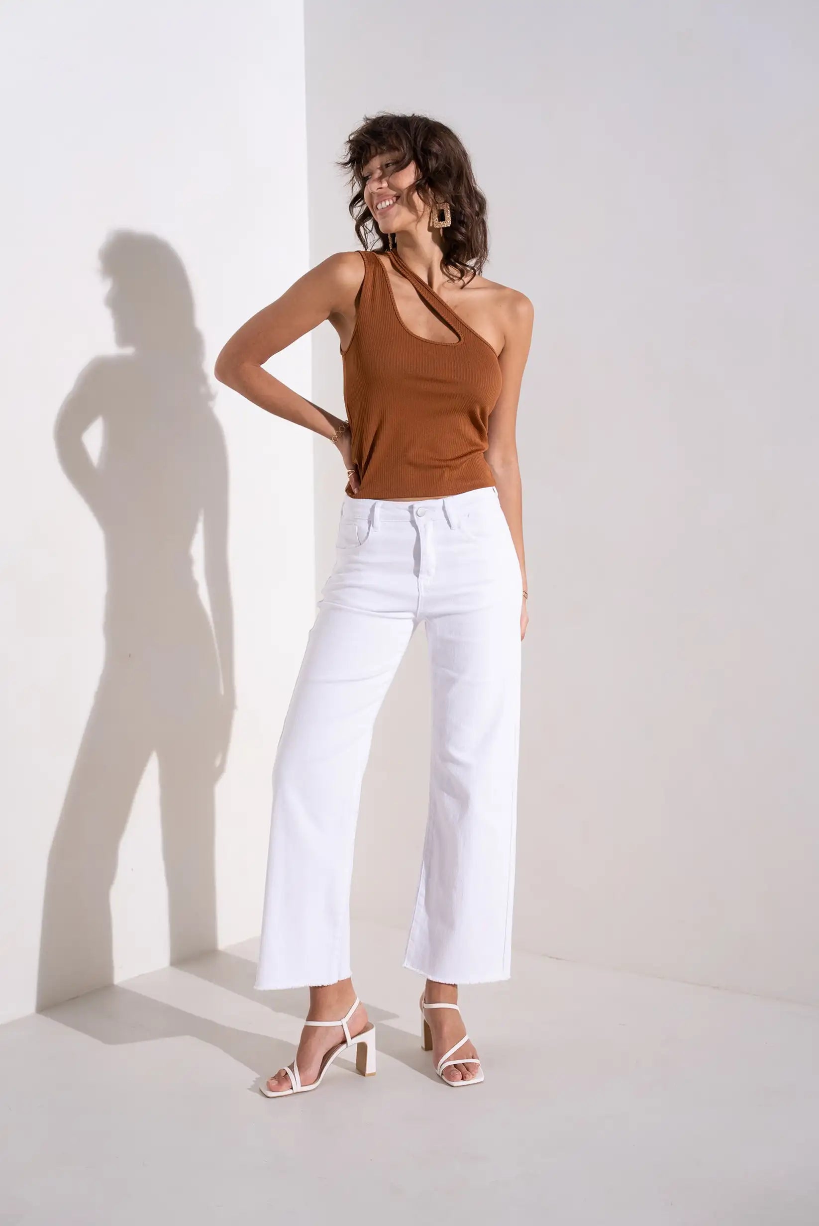 Mujer con pantalón blanco flare y top marrón de tirante, look de primavera moderno