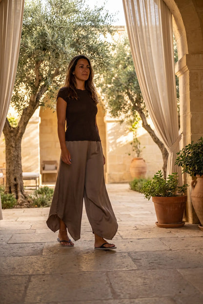 Mujer con pantalón ancho de moda femenina, camiseta y chanclas en patio con olivos y cortinas