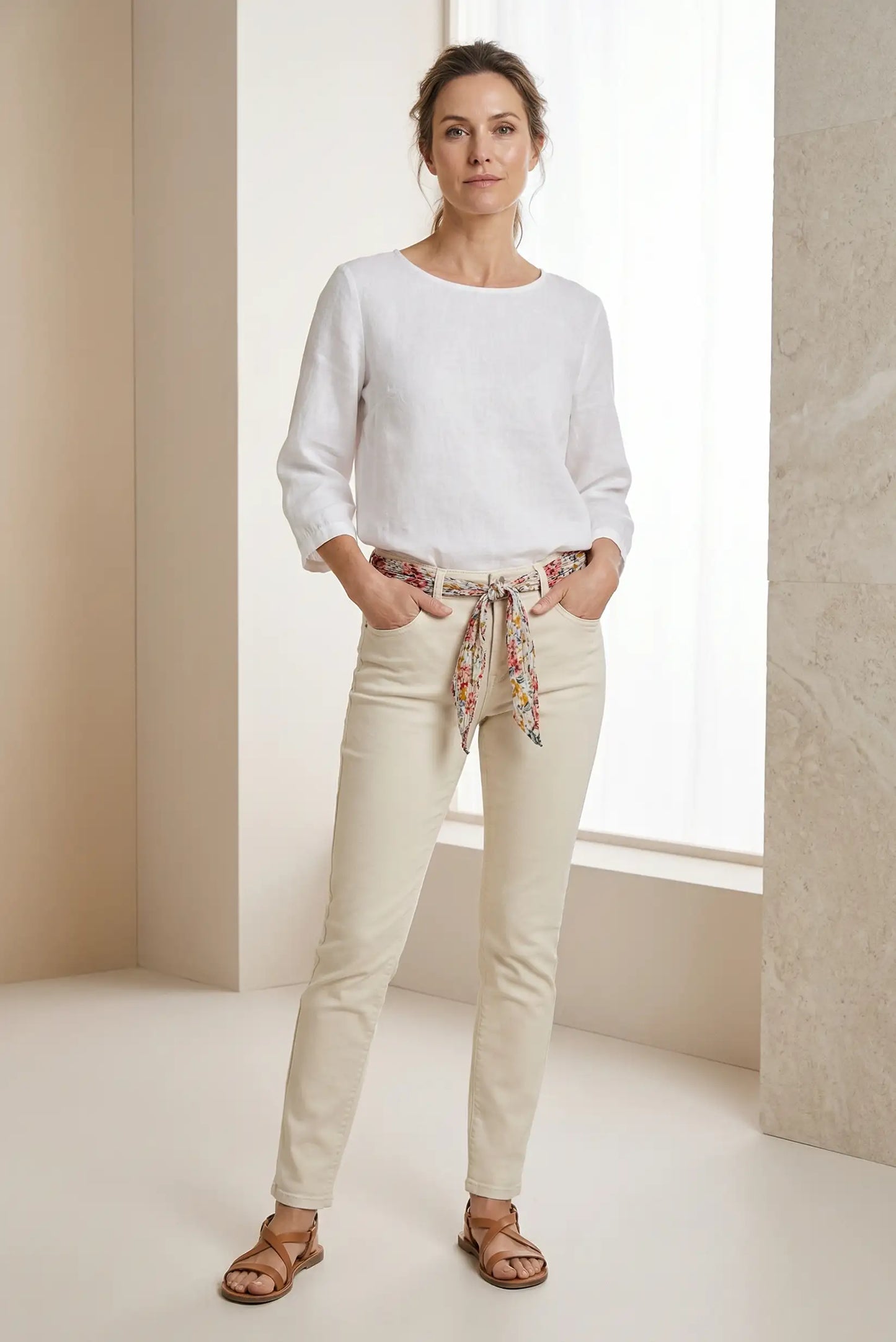 Mujer con pantalón vaquero blanco ajustado, cinturón de tela estampado y blusa blanca, estilo casual.