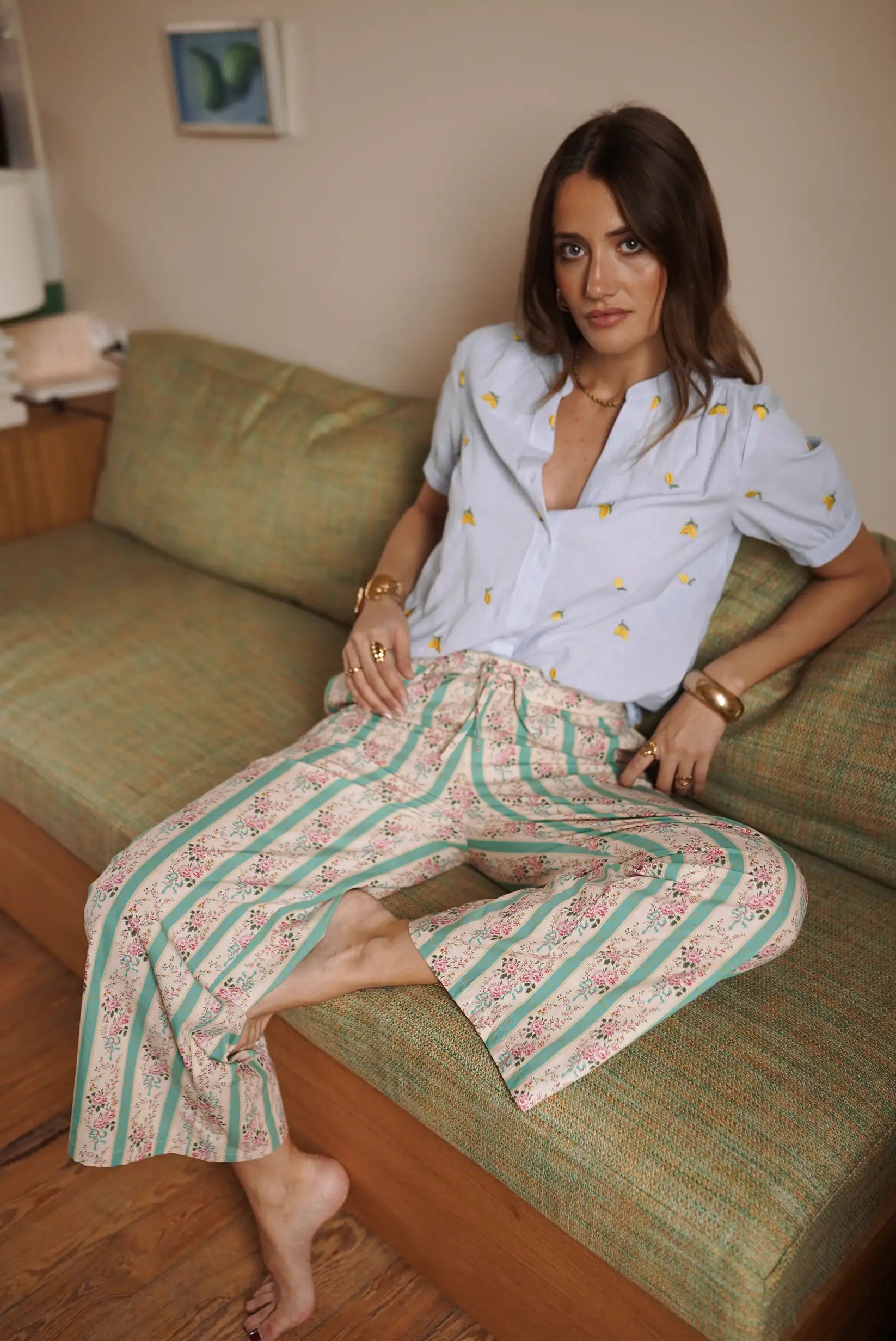 Mujer con pantalón fluido verde de rayas y flores, look casual primaveral, sentada en sofá