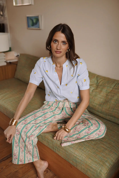 Mujer sentada con pantalón fluido verde de rayas y flores, y blusa azul de manga corta