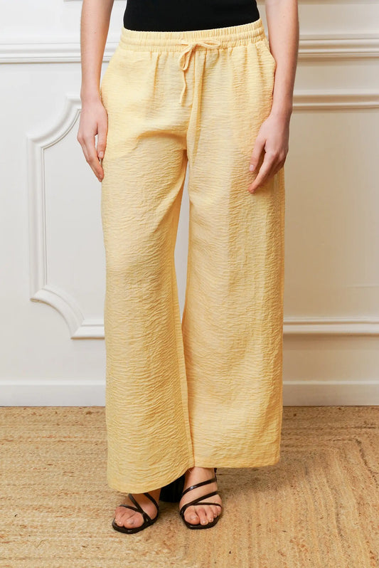 Pantalón largo de mujer amarillo pastel, corte ancho y textura arrugada, estilo primavera