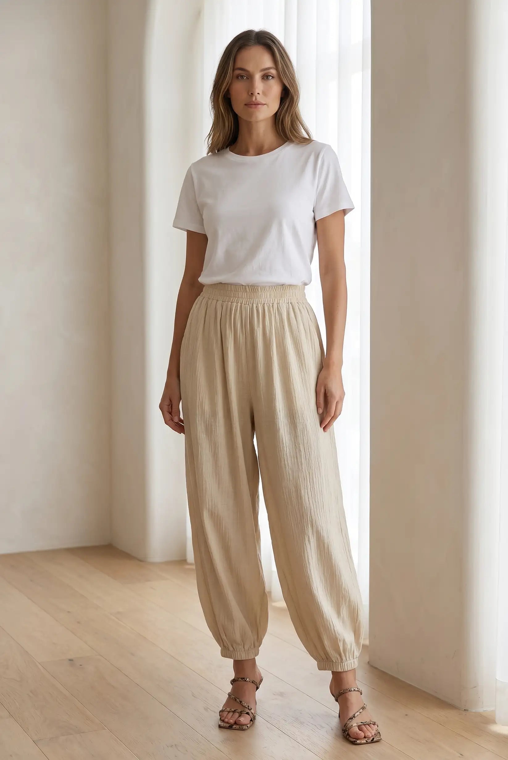 Mujer con pantalón bombacho beige y camiseta blanca, estilo casual, en interior luminoso