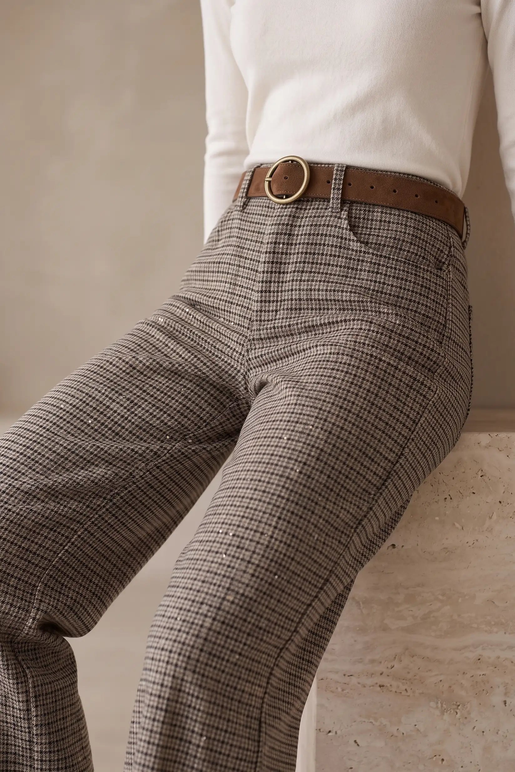 Plano detalle de pantalón de vestir a cuadros marrón con cinturón marrón y hebilla dorada.