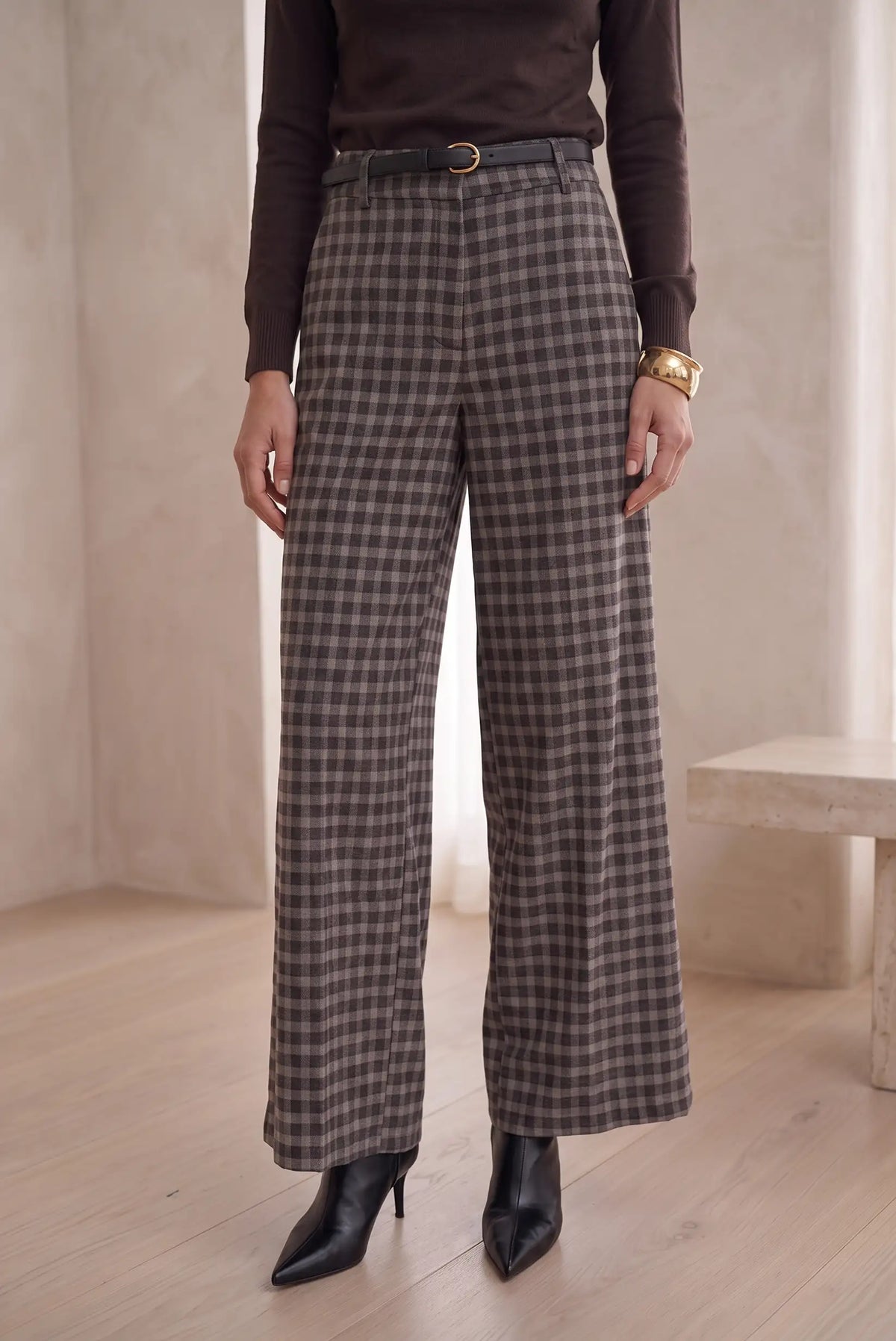 Mujer vistiendo pantalón largo de cuadros en gris y marrón de CHICA del Sur con botines negros.