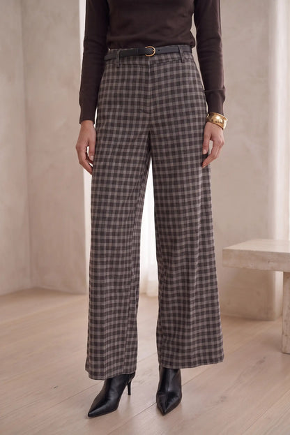 Mujer vistiendo pantalón largo de cuadros en gris y marrón de CHICA del Sur con botines negros.