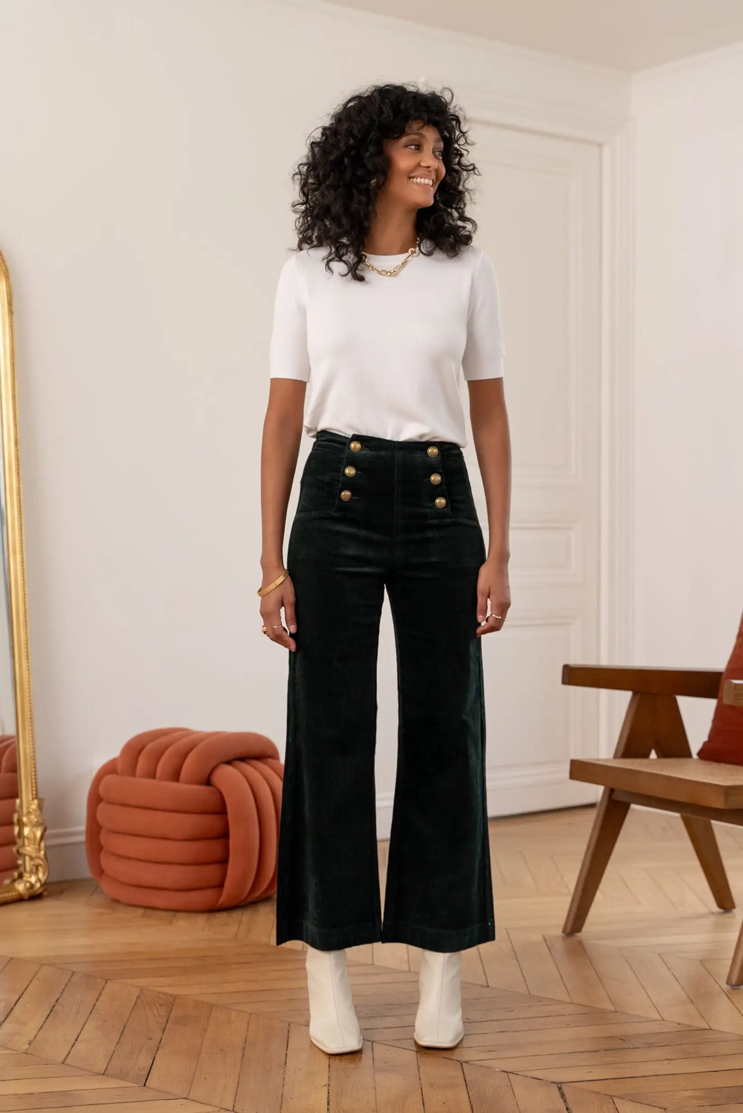 Mujer de pie con pantalón largo alto de micropana verde botella y camiseta blanca en interior moderno