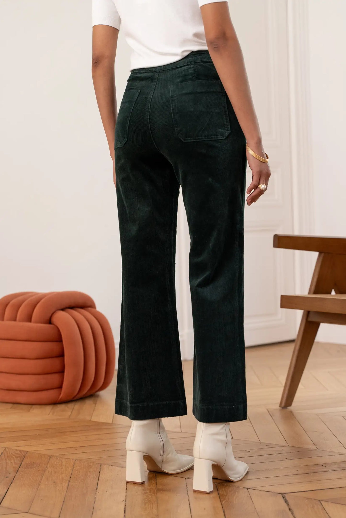 Pantalón largo de micropana verde botella para mujer, con botas blancas y suelo de madera