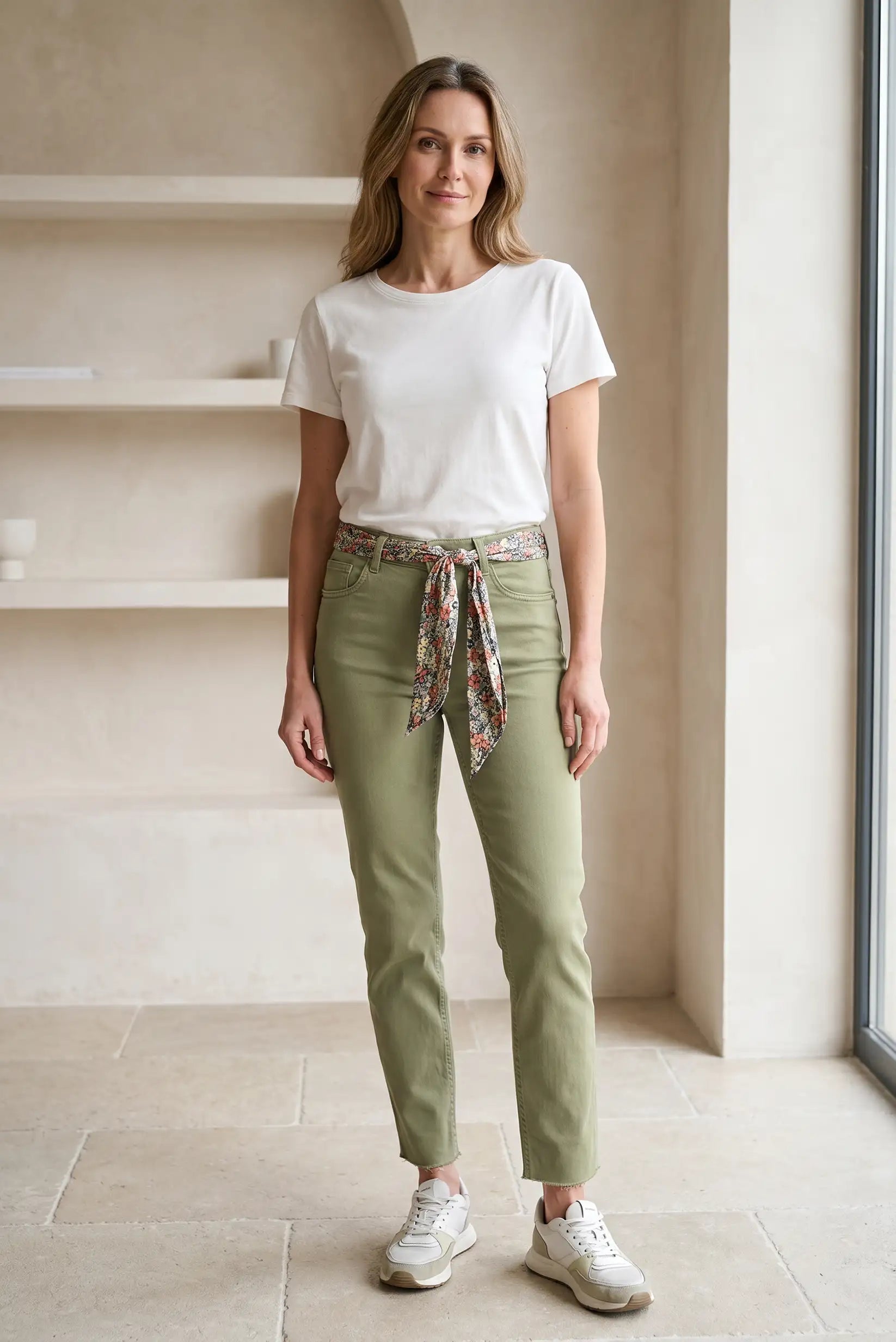Mujer con pantalón pitillo verde oliva y cinturón floral, camiseta blanca y zapatillas