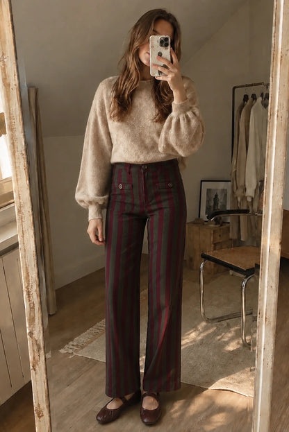 Mujer con jersey beige de manga abullonada y pantalones anchos a rayas granate y negro.