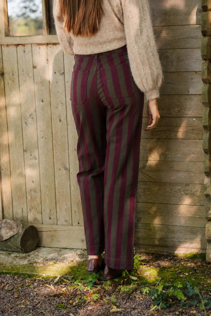 Mujer con pantalones a rayas verticales granates y verdes y jersey beige.