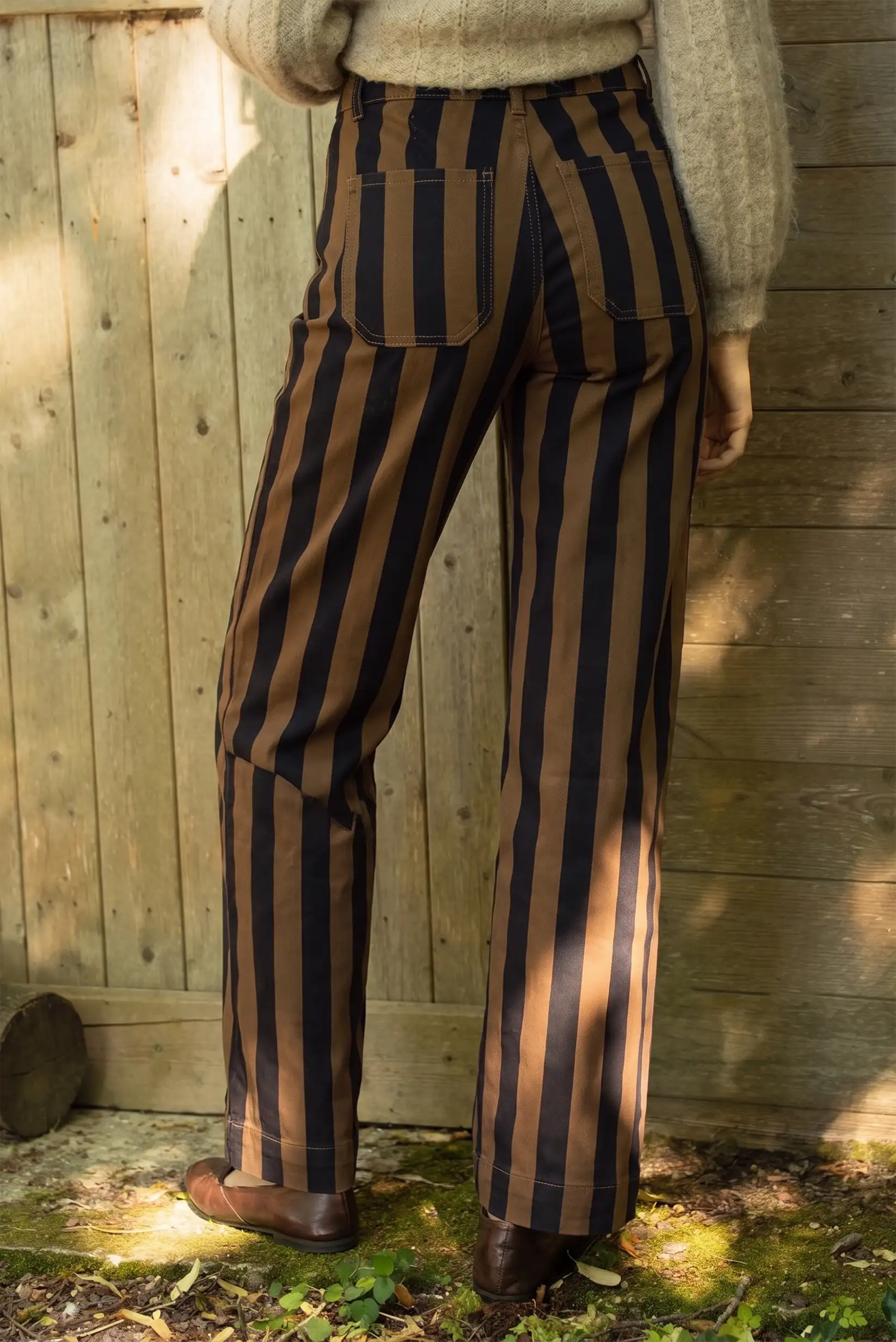 Pantalones de rayas verticales marrón y negro con corte recto y zapato marrón.