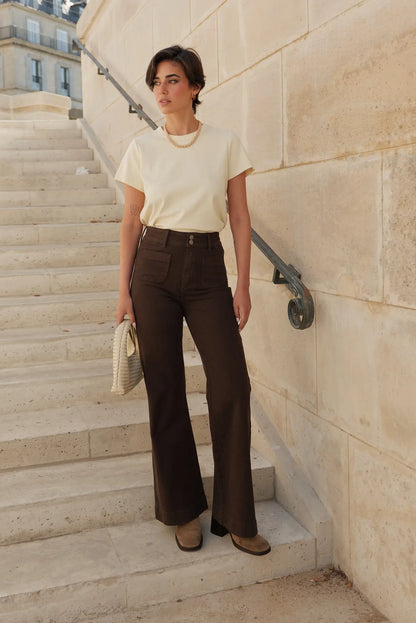 Mujer con pantalón largo vaquero marrón chocolate de 5 bolsillos y camiseta beige en escaleras de piedra