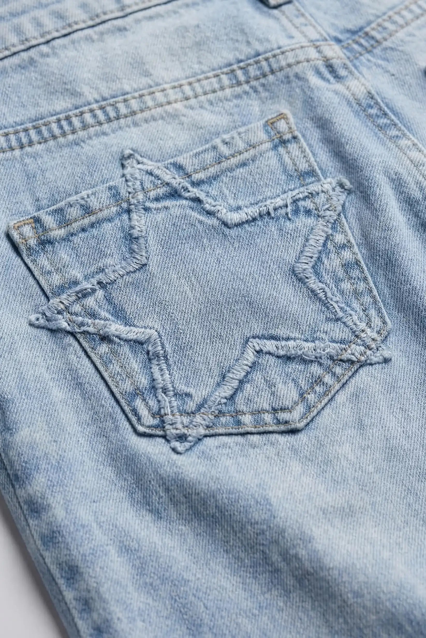 Detalle de bolsillo trasero con estrella en pantalón vaquero azul claro de mujer