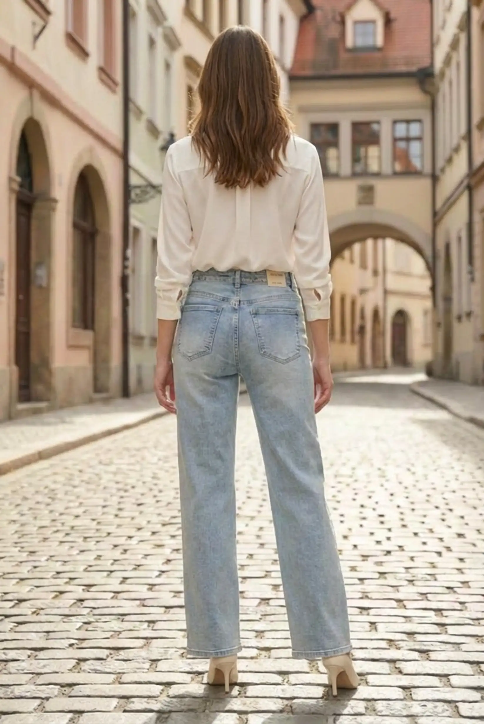 Mujer con pantalón vaquero azul recto y blusa blanca en calle empedrada, moda CHICA del Sur