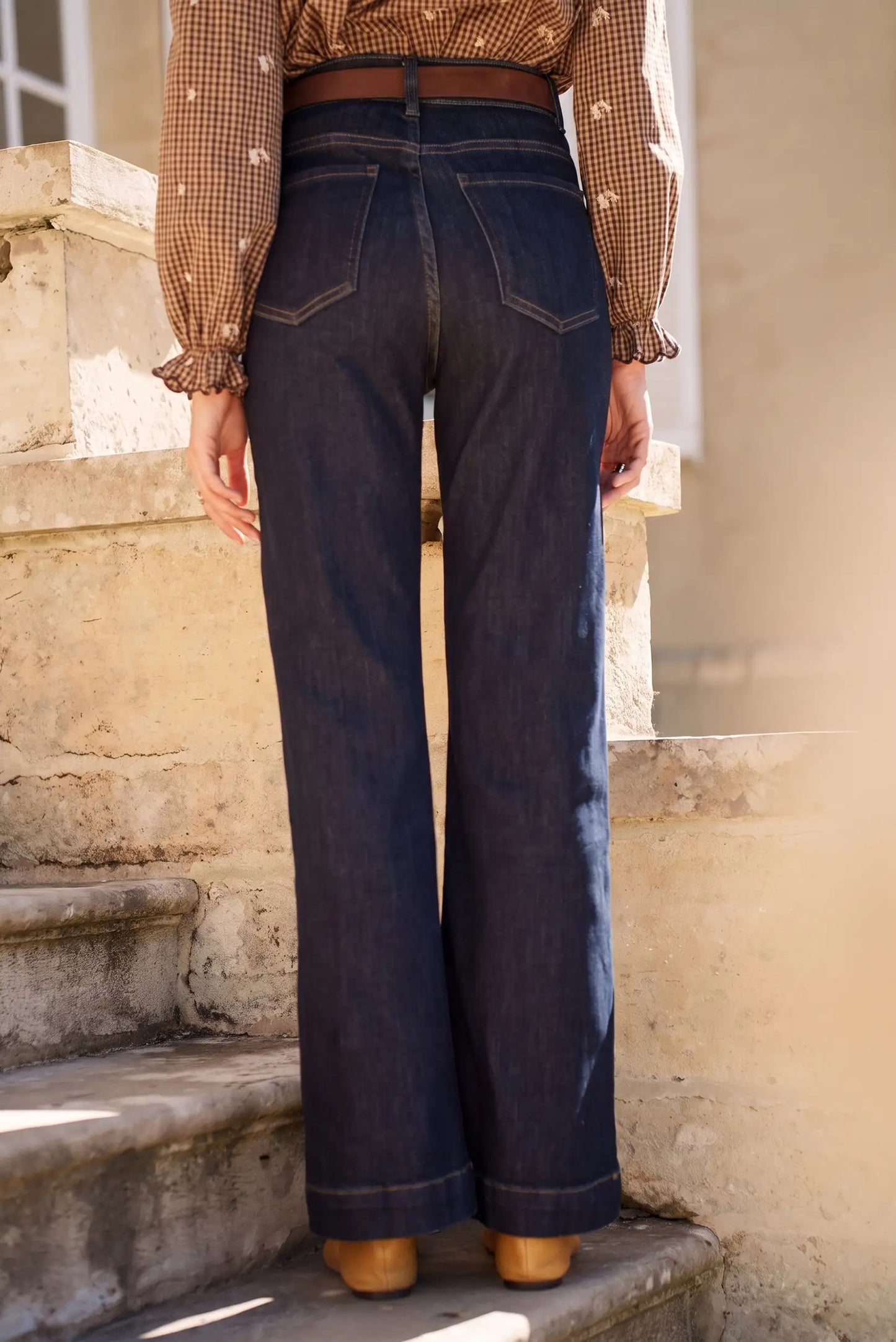 Jeans vaqueros anchos de tiro alto con cinturón marrón, combinados con blusa a cuadros y zapatos marrones en escaleras.
