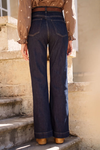 Jeans vaqueros anchos de tiro alto con cinturón marrón, combinados con blusa a cuadros y zapatos marrones en escaleras.