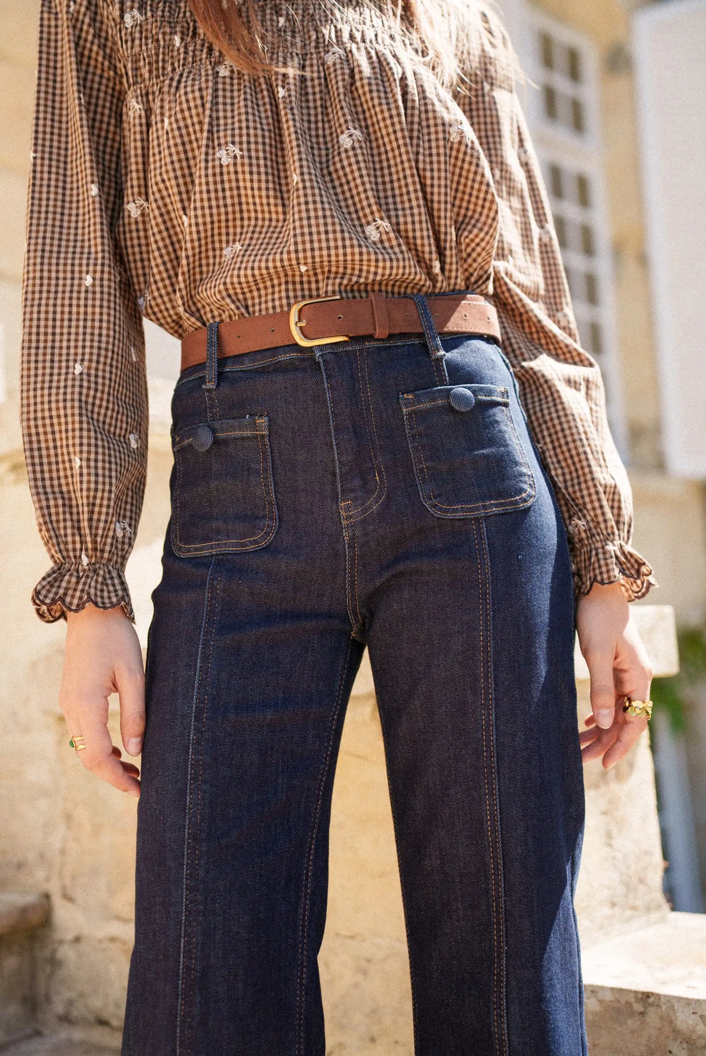 Jeans vaqueros azul oscuro con bolsillos traseros y cinturón marrón, combinados con blusa a cuadros