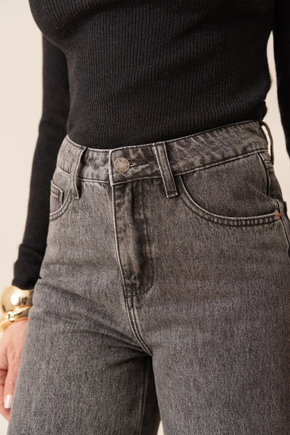 Jeans grises de tiro alto con detalles desgastados, combinados con jersey negro. Moda femenina cómoda y versátil.