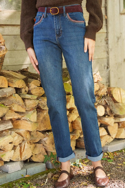 Vaqueros azules rectos con bolsillos decorados, cinturón marrón y zapatos planos, ideal para look casual otoño