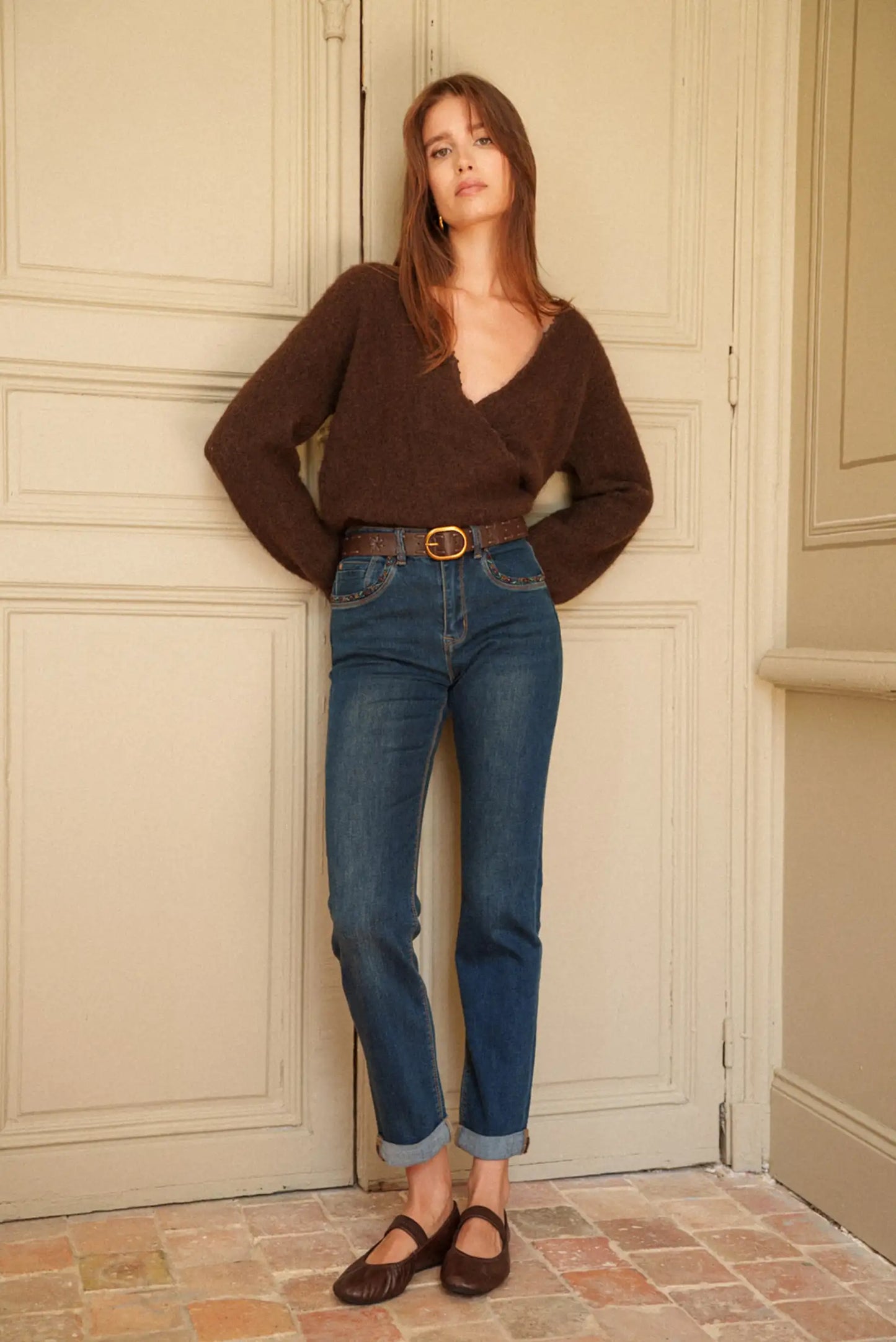 Jeans azul medio con cinturón marrón, suéter de punto y bailarinas. Moda femenina cómoda y elegante.