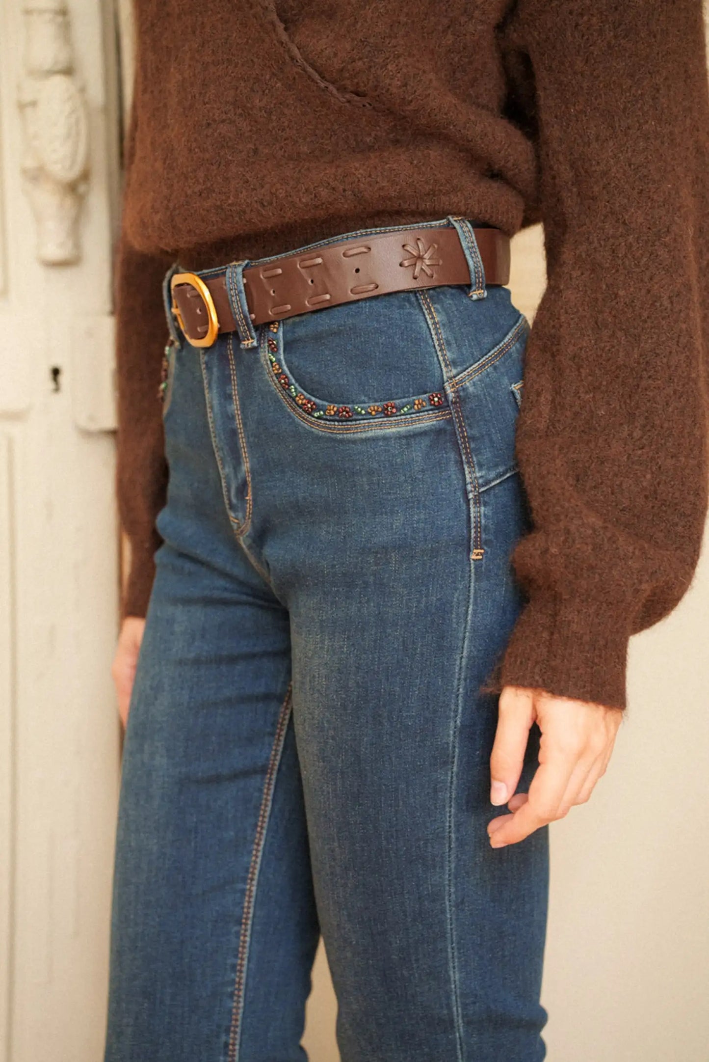 Jeans azul medio con bordado floral en bolsillo, cinturón marrón y suéter marrón, moda femenina