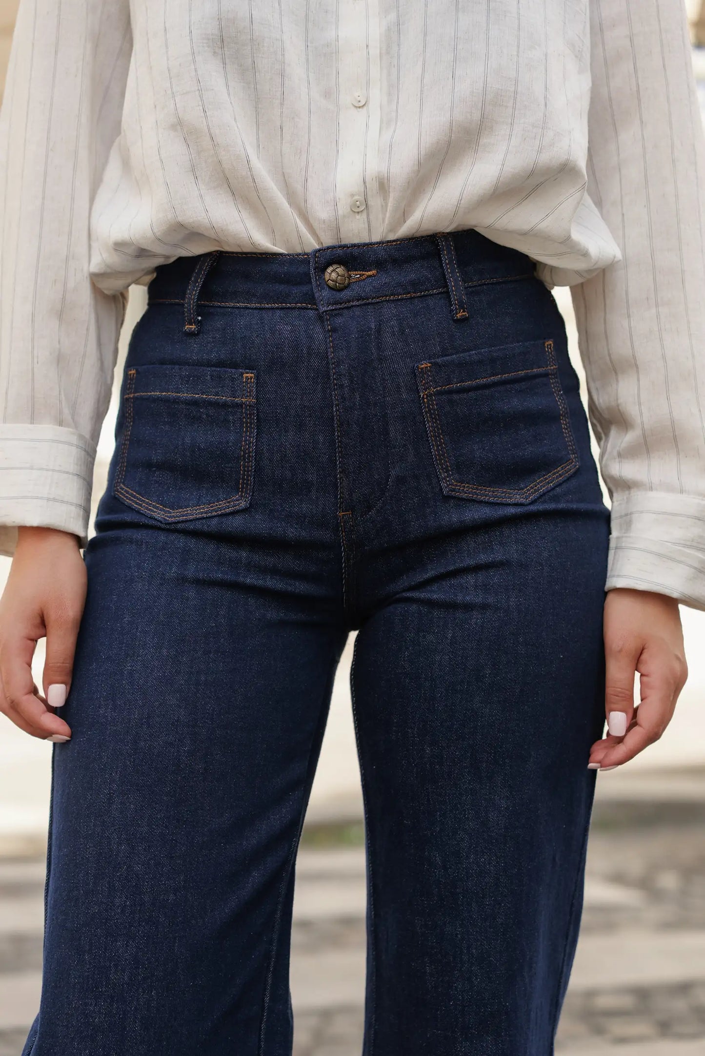Vaqueros azul oscuro con corte recto y costuras en contraste, combinados con blusa de rayas finas. Moda femenina cómoda y versátil.