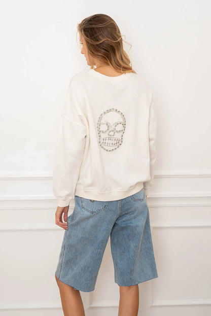Mujer de espaldas con sudadera blanca con calavera de pedrería y bermudas vaqueras claras.