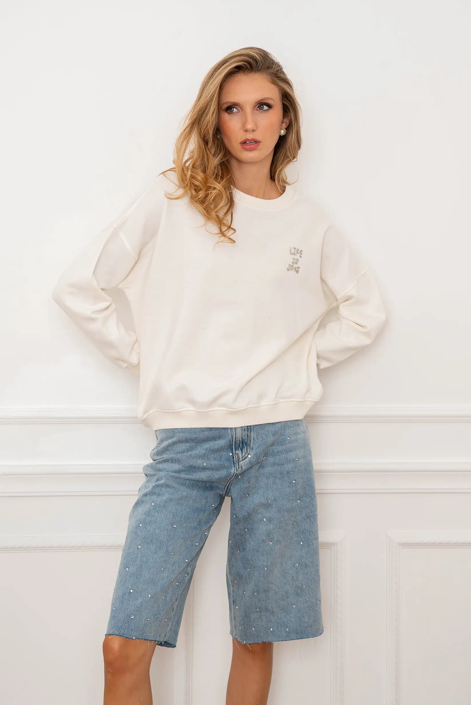 Mujer con sudadera blanca oversize y bermudas vaqueras con brillantes.
