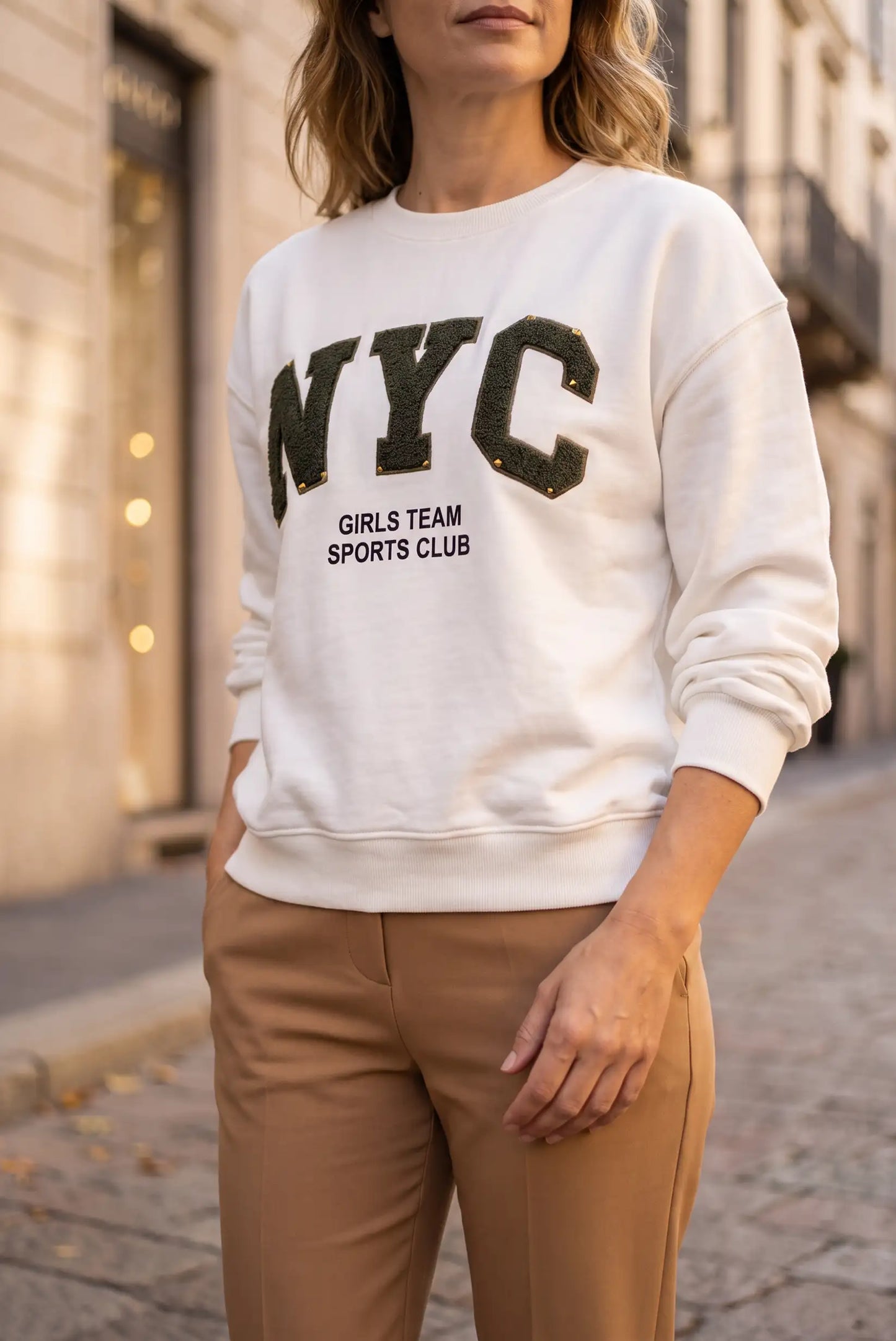 Mujer vistiendo sudadera blanca con letras NYC verdes y pantalones beige