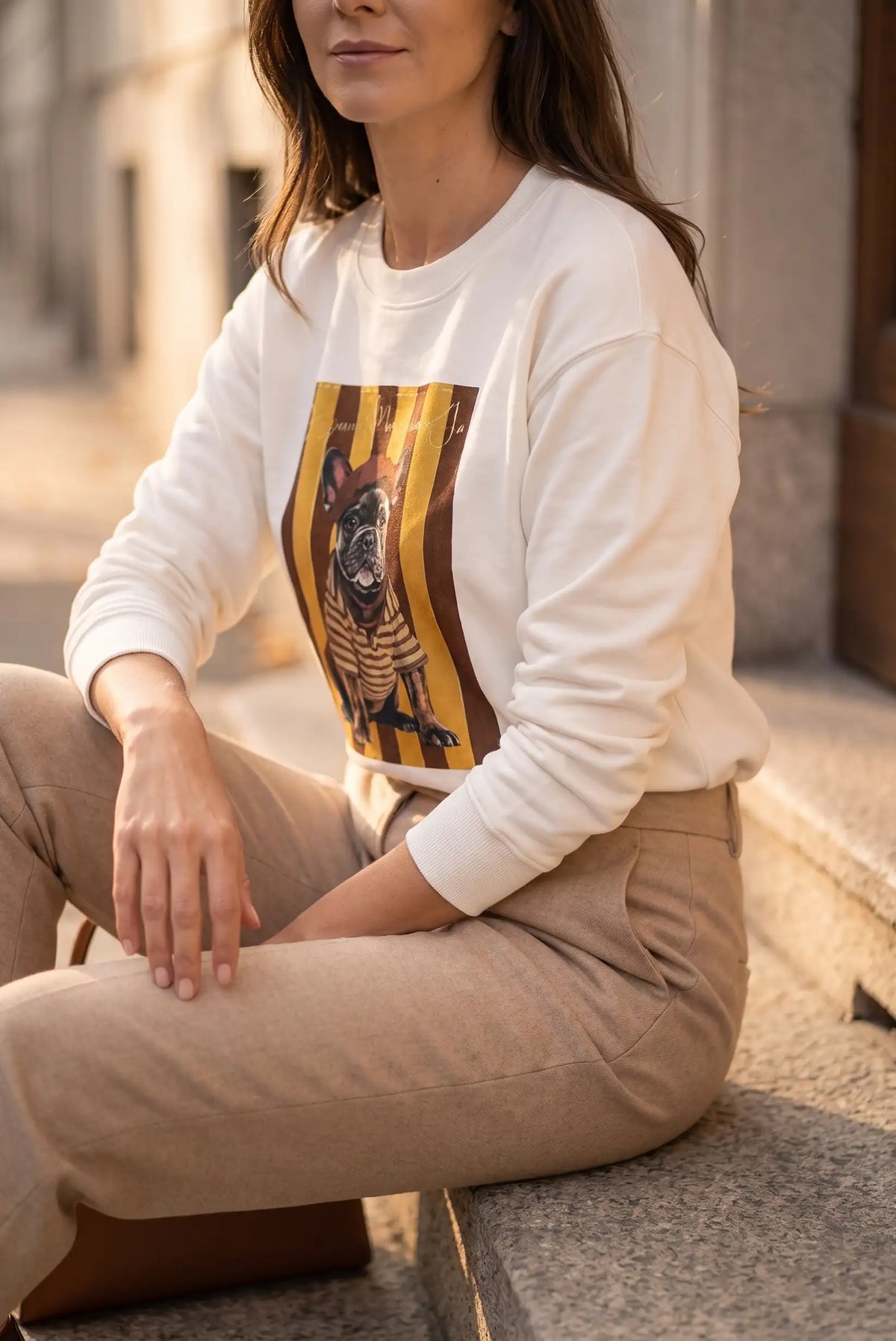 Mujer sentada con sudadera blanca con estampado de bulldog francés y pantalones beige.