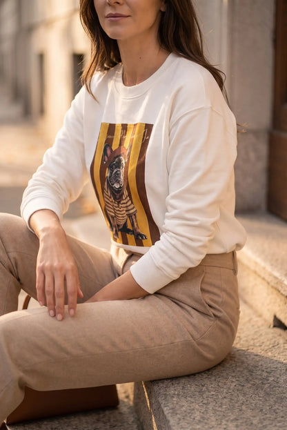 Mujer sentada con sudadera blanca con estampado de bulldog francés y pantalones beige.