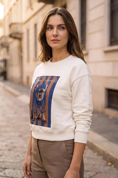 Mujer joven vistiendo sudadera blanca con estampado de bulldog francés en una calle urbana.