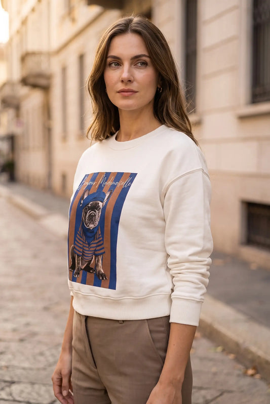 Mujer joven vistiendo sudadera blanca con estampado de bulldog francés en una calle urbana.