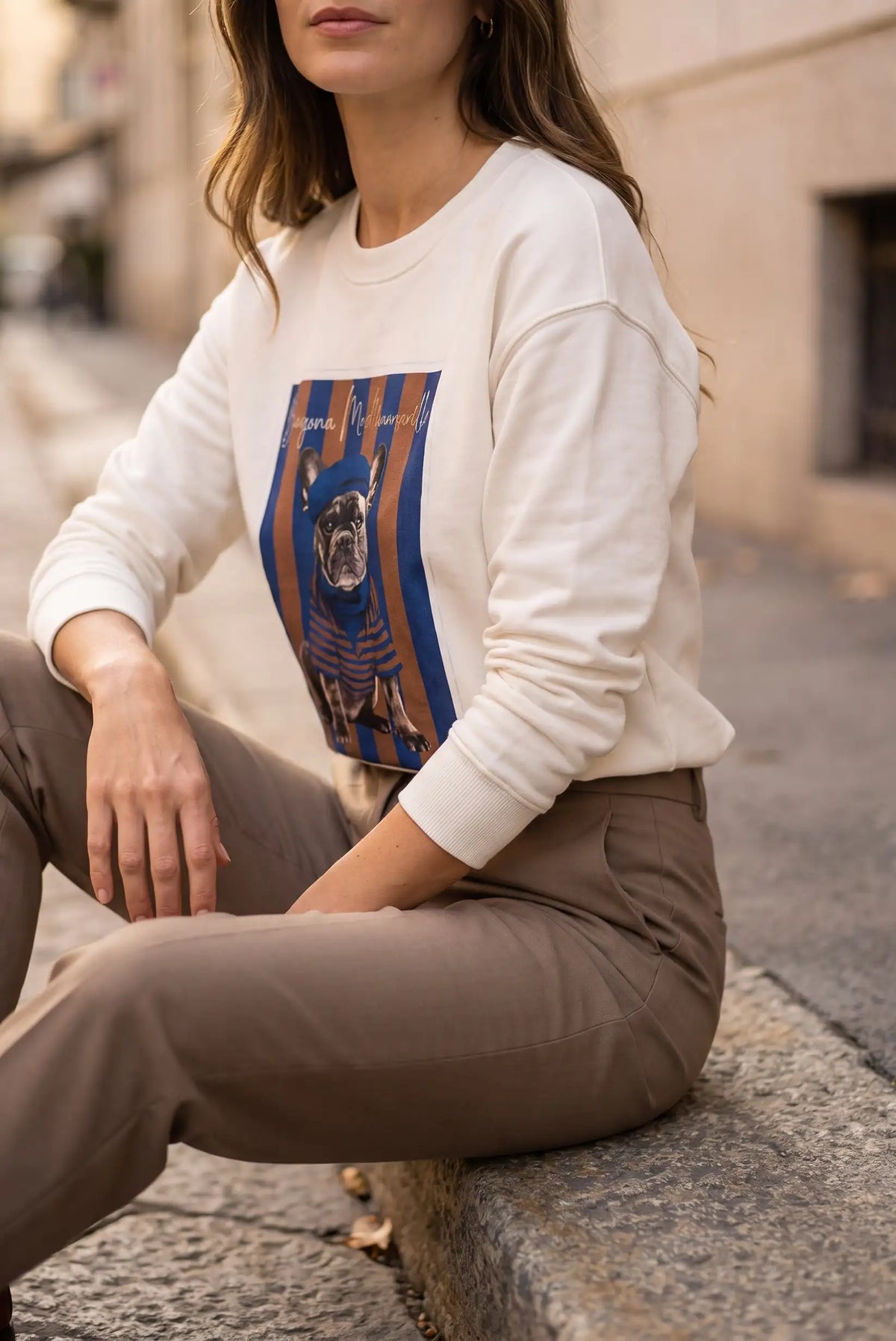 Mujer con sudadera blanca con estampado de bulldog francés y pantalones beige.