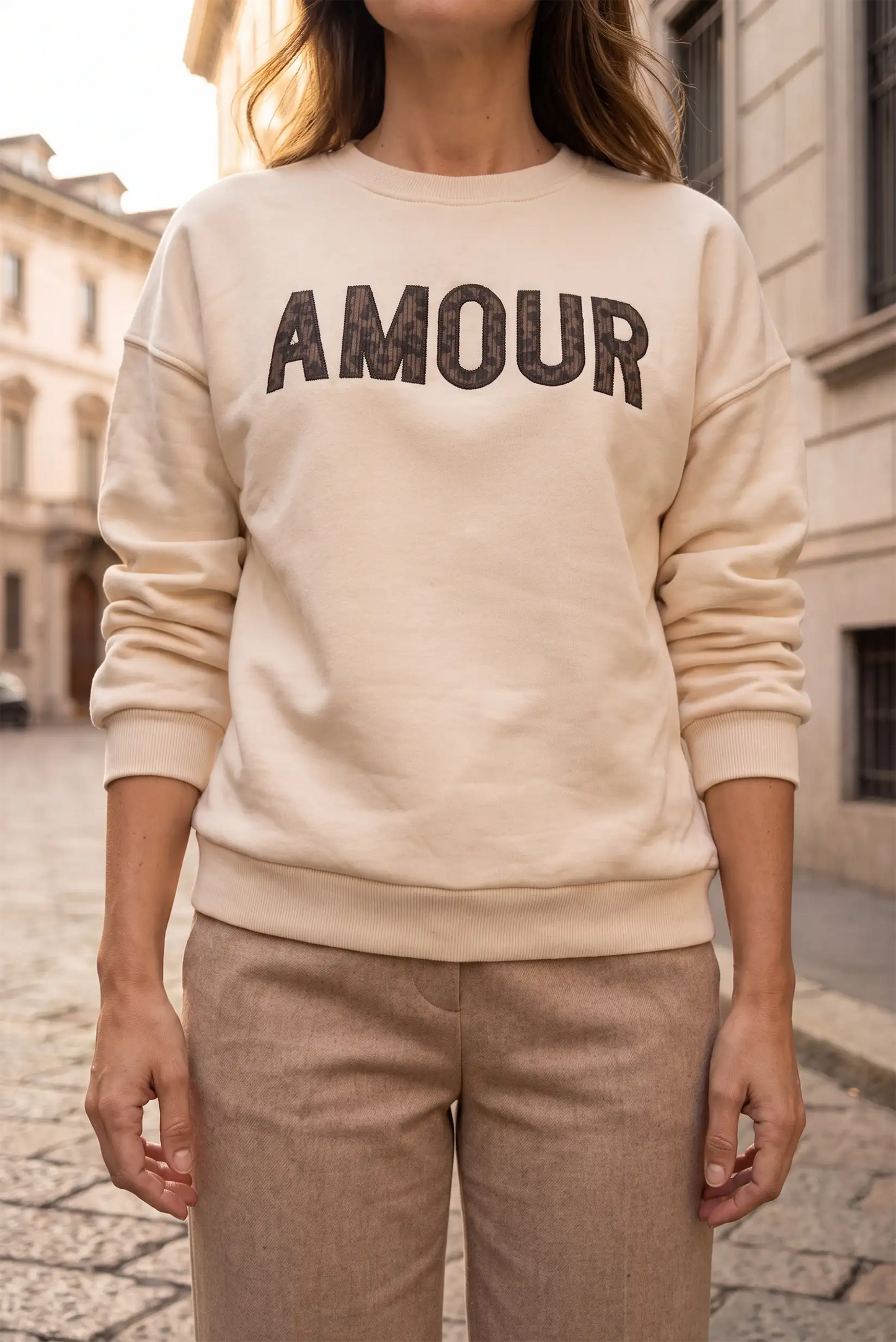 Mujer vistiendo sudadera beige con la palabra AMOUR en letras oscuras y pantalones marrones.