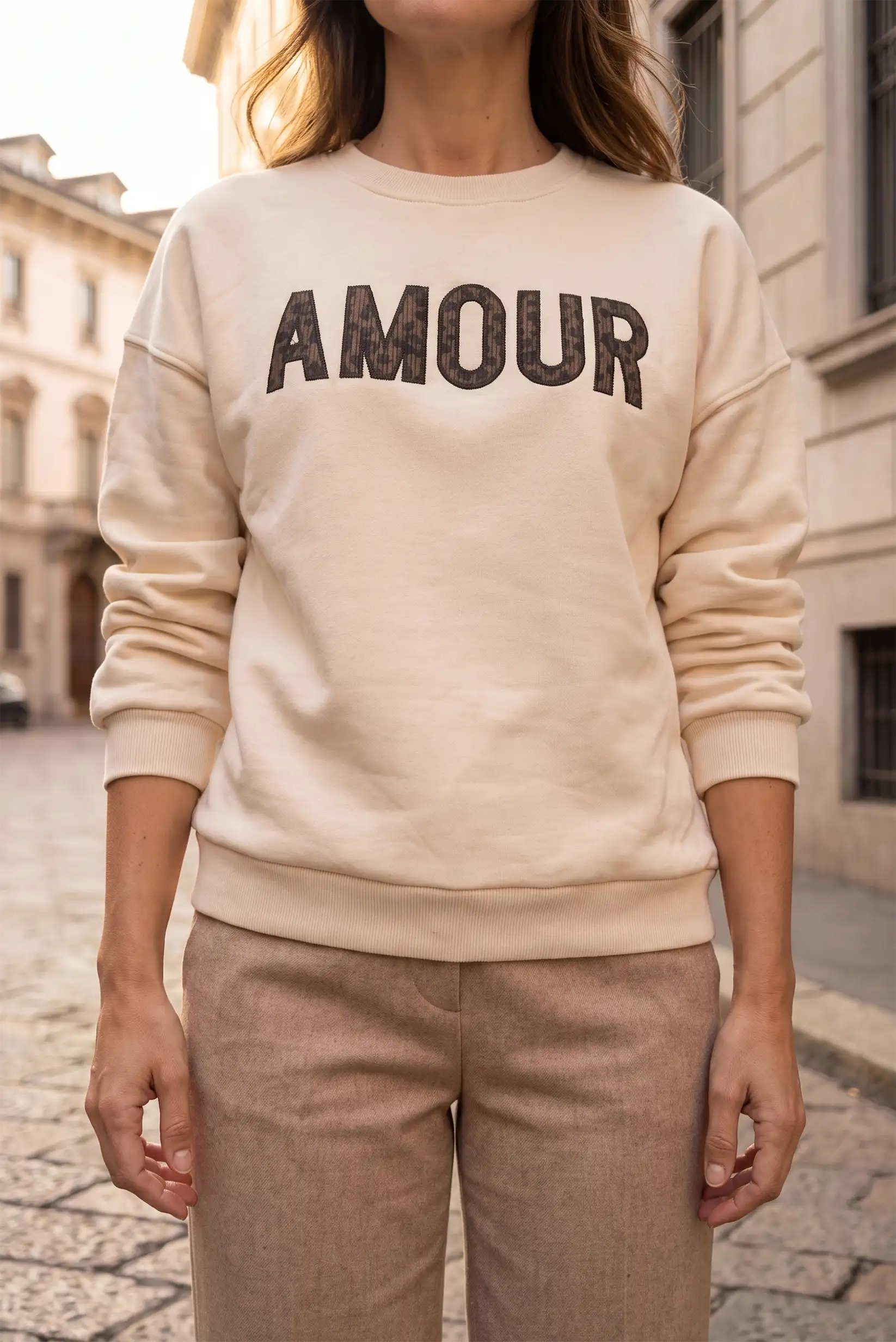 Mujer vistiendo sudadera beige con la palabra AMOUR en letras oscuras y pantalones marrones.